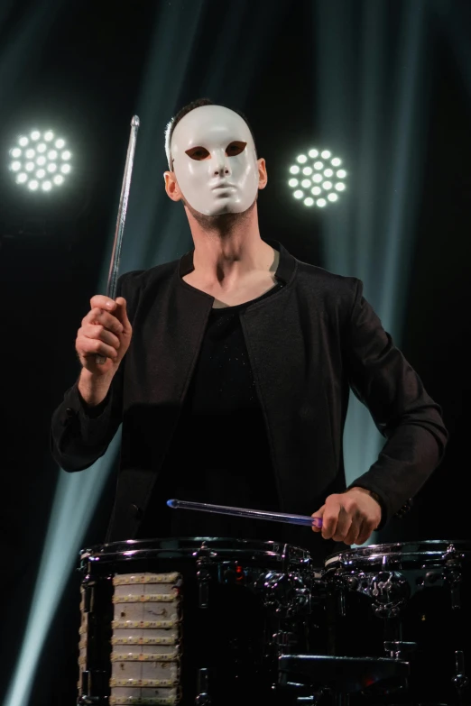 a man in a white mask playing drums, by Julia Pishtar, antipodeans, perfect face symmetry, skinny male magician, promo image, cheekbones