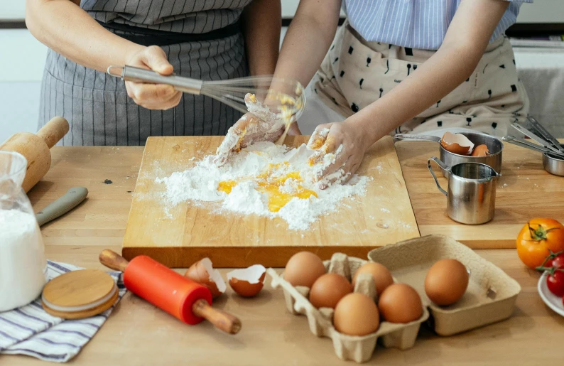a couple of women standing next to each other in a kitchen, trending on pexels, process art, ingredients on the table, eggs, square, background image