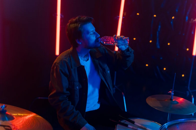 a man that is sitting in front of a drum set, holding a drink, orelsan, vfx shot, cinematic blue lighting