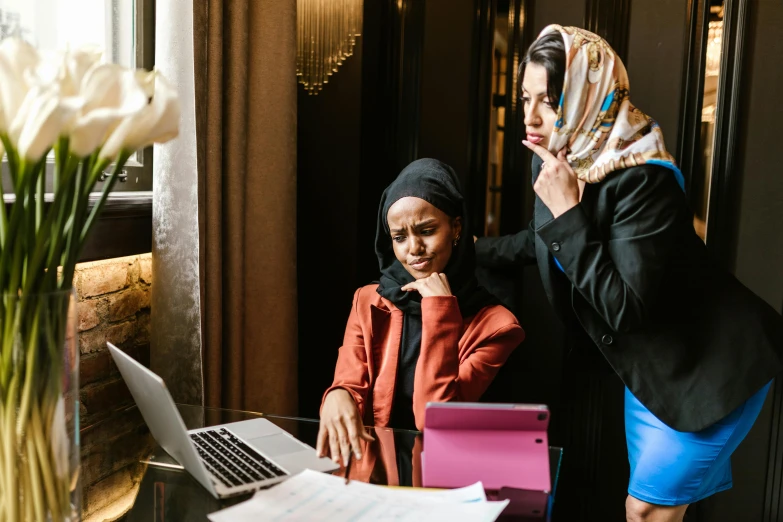 two women standing next to each other in front of a laptop, by Julia Pishtar, pexels contest winner, hurufiyya, concerned expression, wearing robes and neckties, wearing a head scarf, woman in business suit