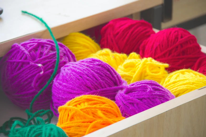 a box filled with lots of colorful balls of yarn, a portrait, inspired by Toss Woollaston, trending on pexels, purple and yellow, medium close shot, looking left, a wooden