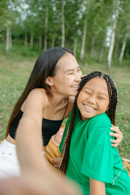 a woman sitting next to a little girl in a field, joy ang, green colored skin, smiling down from above, hugging