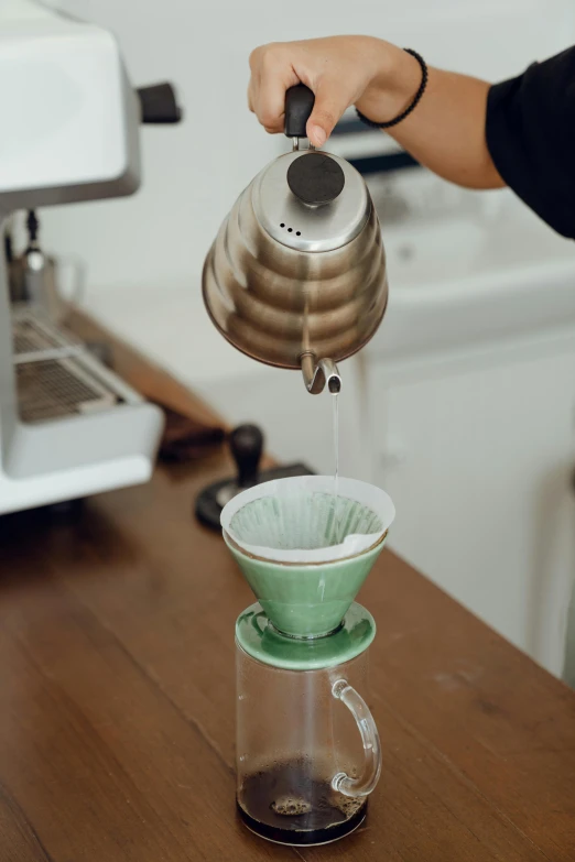 a person pours water into a coffee pot, by Matthias Stom, trending on unsplash, starbucks aprons and visors, green, detailed product image, cone shaped