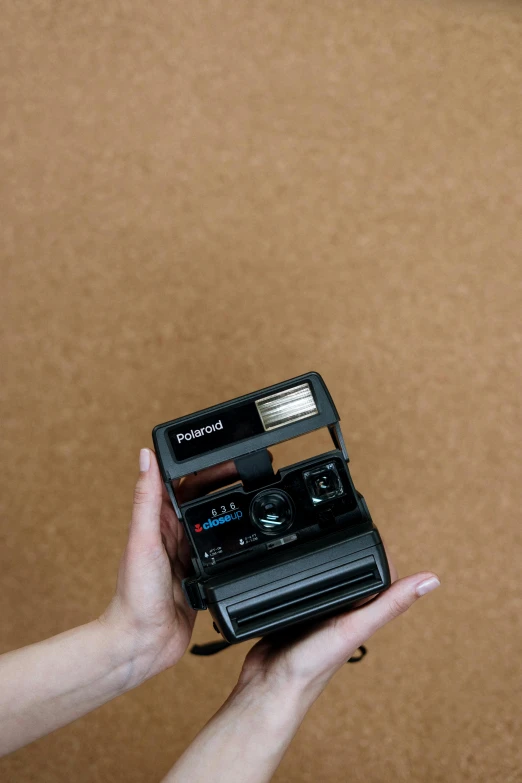 a person holding a polaroid camera in their hand, inspired by Nan Goldin, unsplash, detailed product image, hasselblad photo, brown, plain background
