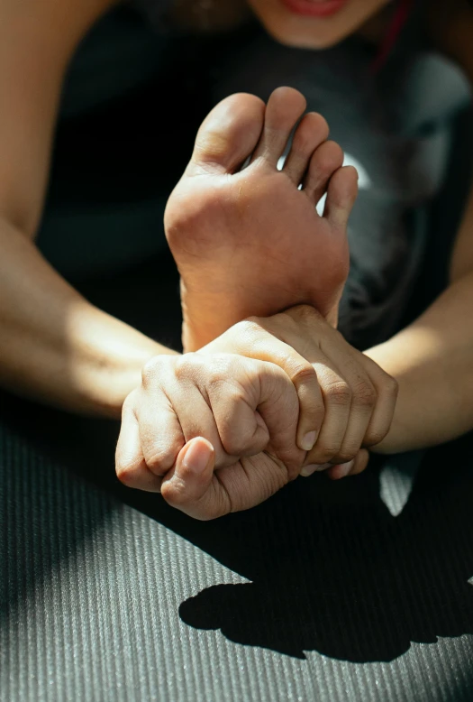 a close up of a person's feet on a mat, with a hurt expression, across holding a hand, square, dynamic stretching