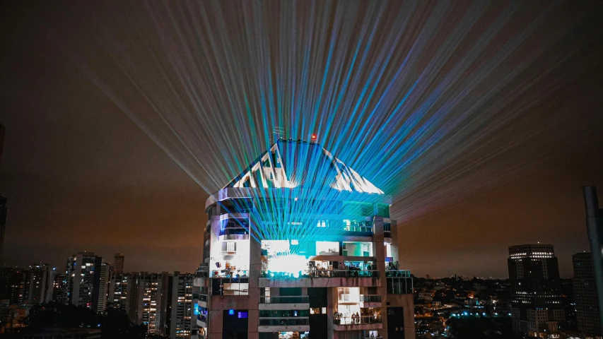 a very tall building with a lot of lights on it, a hologram, by Lee Loughridge, unsplash contest winner, holography, laser turret, rooftop party, felipe pantone, beams of light from sky