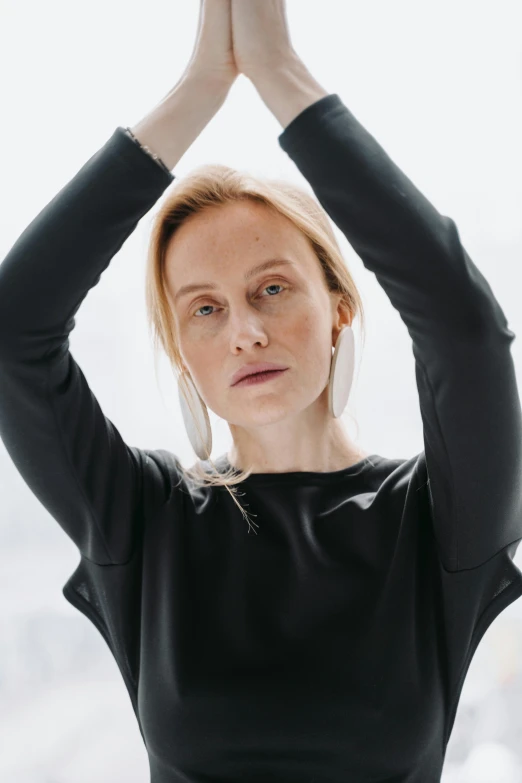 a woman doing a yoga pose in front of a window, a portrait, inspired by Louisa Matthíasdóttir, trending on unsplash, black sweater, set against a white background, pale complexion, looking serious