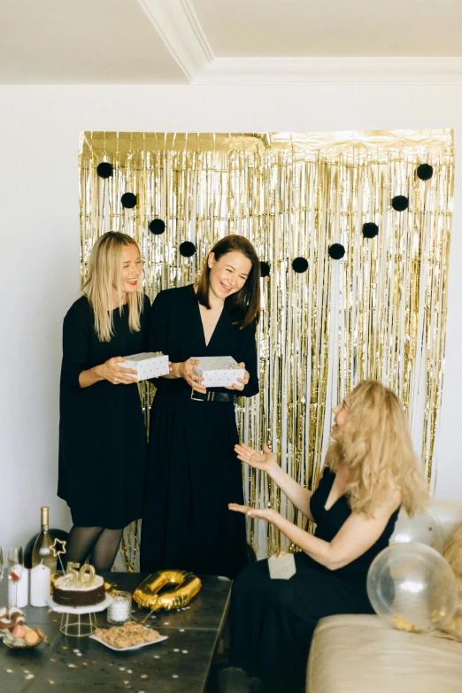 a group of women standing next to each other in a living room, by Julia Pishtar, pexels contest winner, black marble and gold, at a birthday party, in front of white back drop, presenting wares