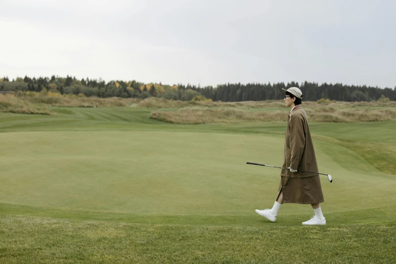 a man walking across a lush green golf course, an album cover, unsplash, bauhaus, wearing hunter coat, baggy clothing and hat, thumbnail, burberry