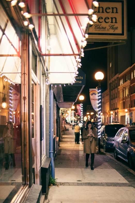a person walking down a city street at night, storefronts, pittsburgh, chic, canopies
