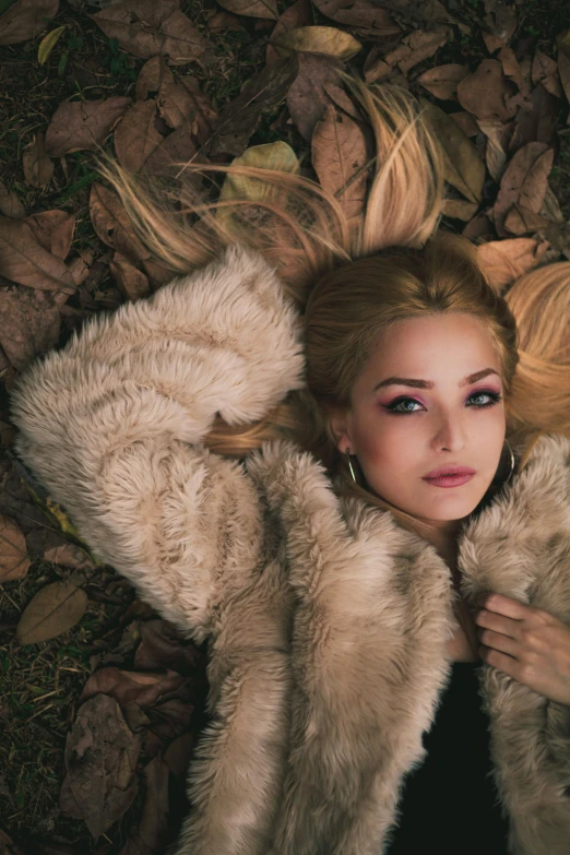 a woman laying on top of a pile of leaves, an album cover, inspired by Elsa Bleda, trending on pexels, renaissance, blond fur, handsome girl, fur coat, high angle shot