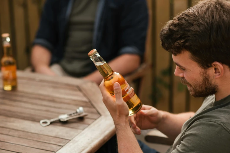 a man sitting at a table holding a bottle of beer, pexels contest winner, half turned around, mead, light tan, matt finish