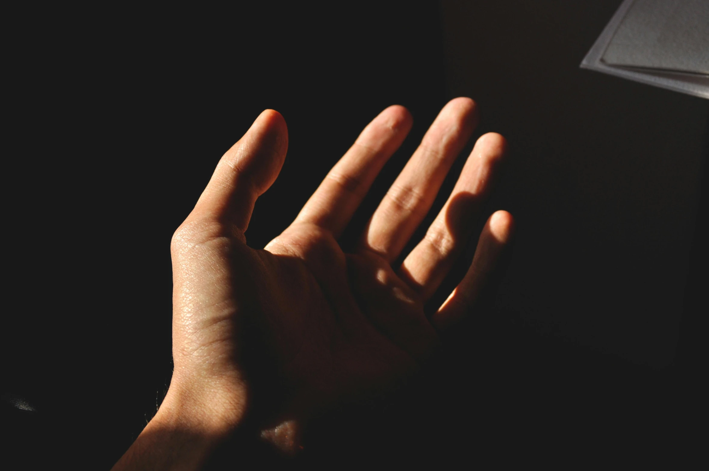 a close up of a person's hand reaching for something, unsplash, light and space, against a deep black background, instagram post, warm light, 4-dimensional