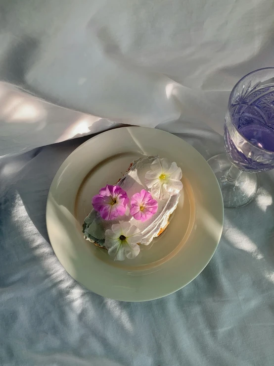 a white plate topped with flowers next to a glass of water, in style of petra collins, cake, ilustration, trending photo