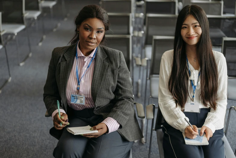 two women sitting next to each other in chairs, trending on pexels, academic art, standing in class, convention photo, uk, conservatively dressed