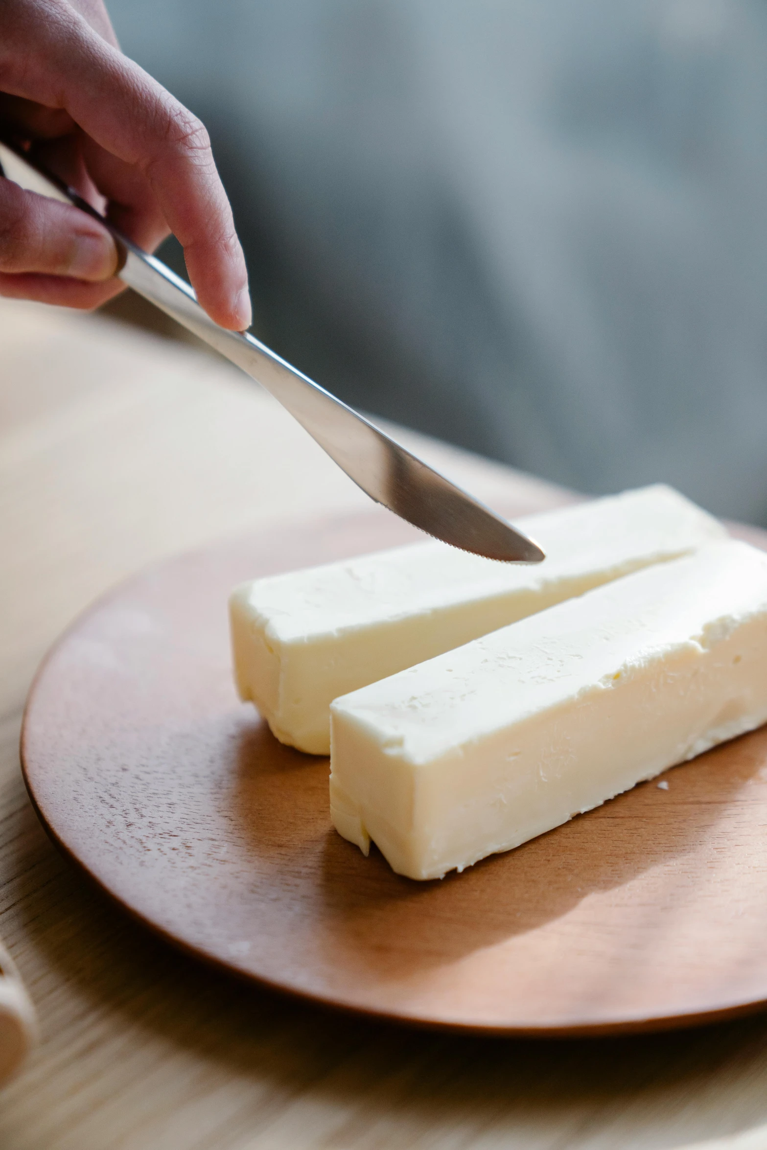 a person cutting a piece of butter on a plate, by Jessie Algie, soft white rubber, on a wooden tray, meaty, long