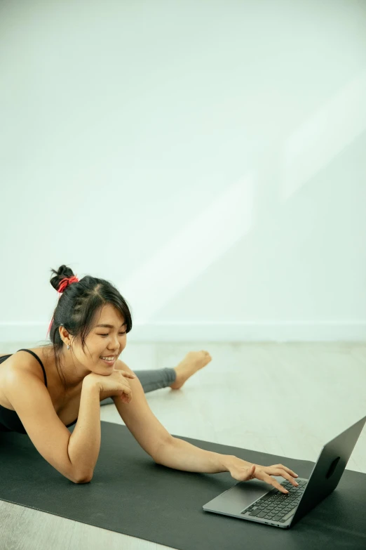 a woman laying on a yoga mat with a laptop, pexels contest winner, an asian woman, streaming on twitch, low quality photo