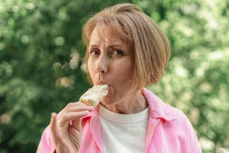 a woman in a pink jacket eating a piece of food, a portrait, by Ellen Gallagher, pexels contest winner, shaven, middle age, on a hot australian day, cake
