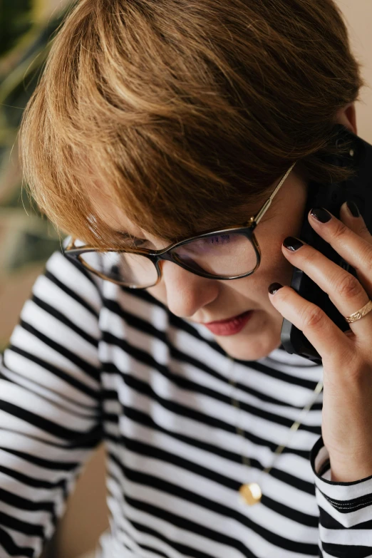 a woman in a striped shirt talking on a cell phone, trending on pexels, sophia lillis, rounded eyeglasses, working in a call center, romantic lead