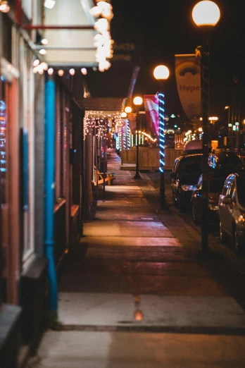 a city street lined with parked cars at night, by Matt Cavotta, trending on unsplash, christmas lights, outside a saloon, location [ chicago ( alley ) ], street of teal stone