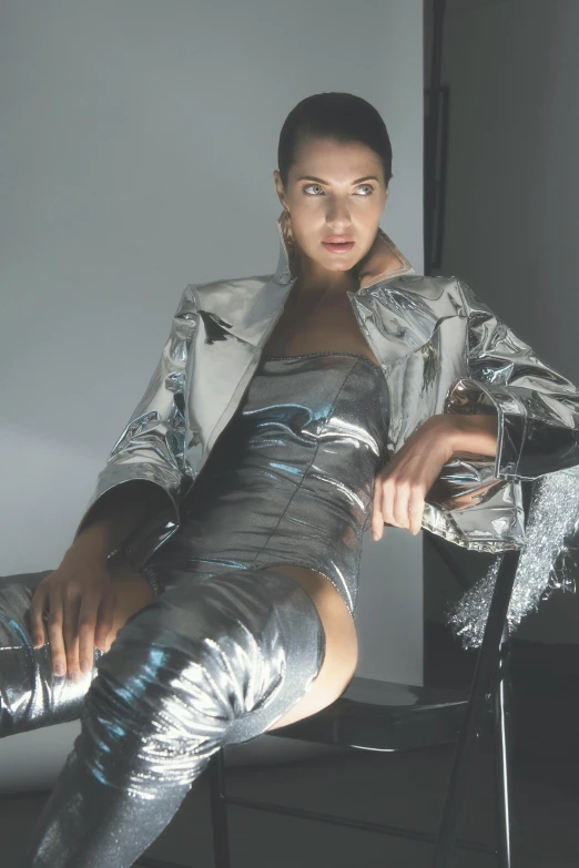 a woman sitting on top of a chair next to a chair, inspired by hajime sorayama, holography, silver metallic moncler jacket, adriana lima, wearing tight suit, zoomed in