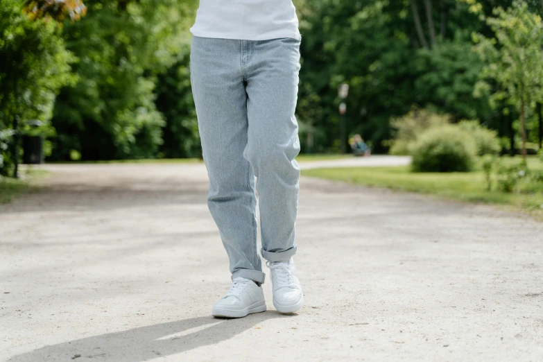 a woman walking down a dirt road while talking on a cell phone, inspired by Peter de Sève, happening, blue jeans and grey sneakers, made in tones of white and grey, in the park, baggy jeans