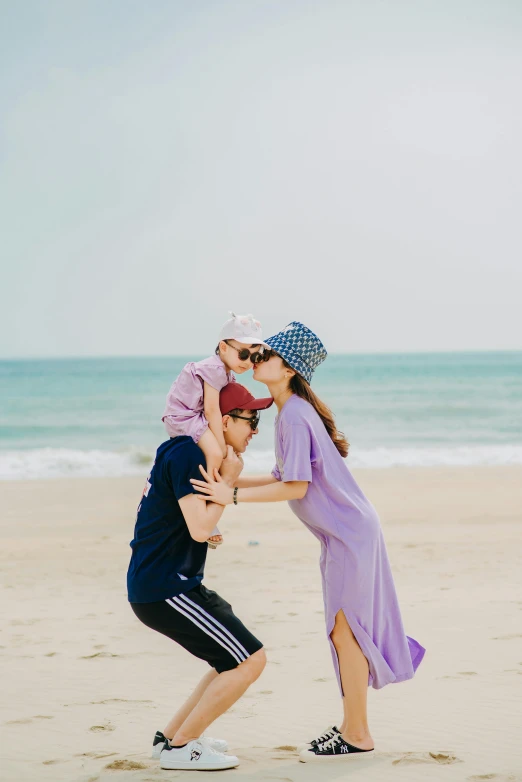 a couple of people standing on top of a sandy beach, wearing a purple cap, with a kid, hong soonsang, playful pose