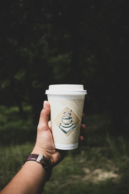 a person holding a cup of coffee in their hand, in front of a forest background, avatar image, promo image, paper cup