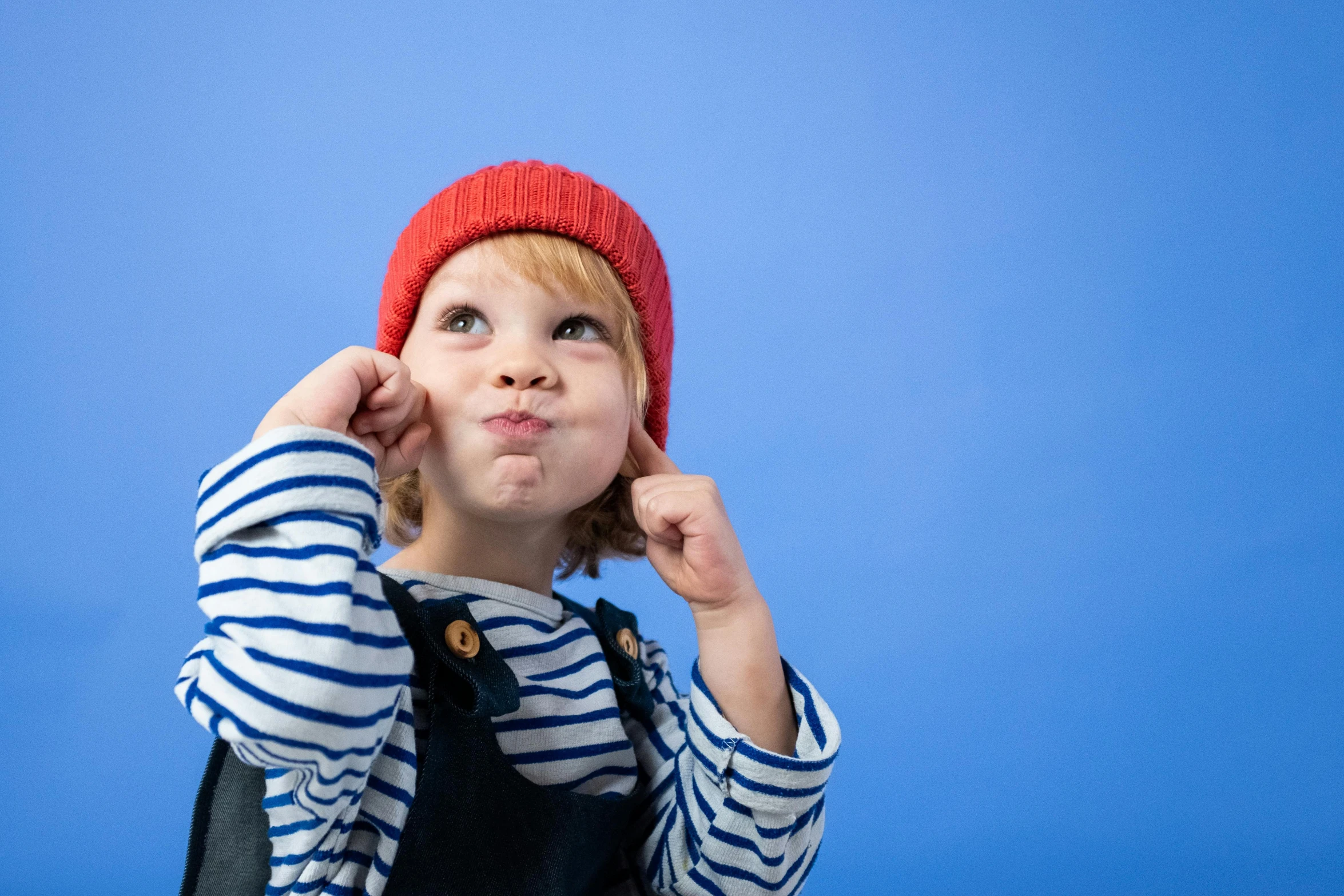 a little boy wearing a striped shirt and a red hat, inspired by Kate Greenaway, trending on pexels, blue backdrop, surprised, french kiss, looking upwards