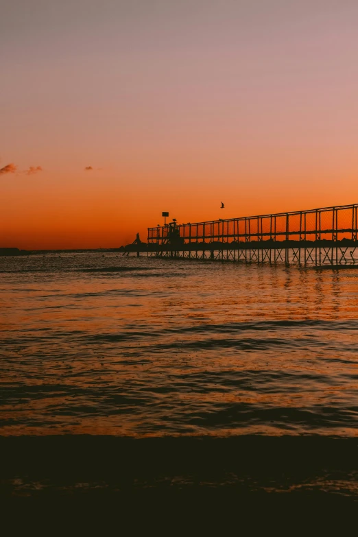 a bridge over a body of water at sunset, on the beach during sunset