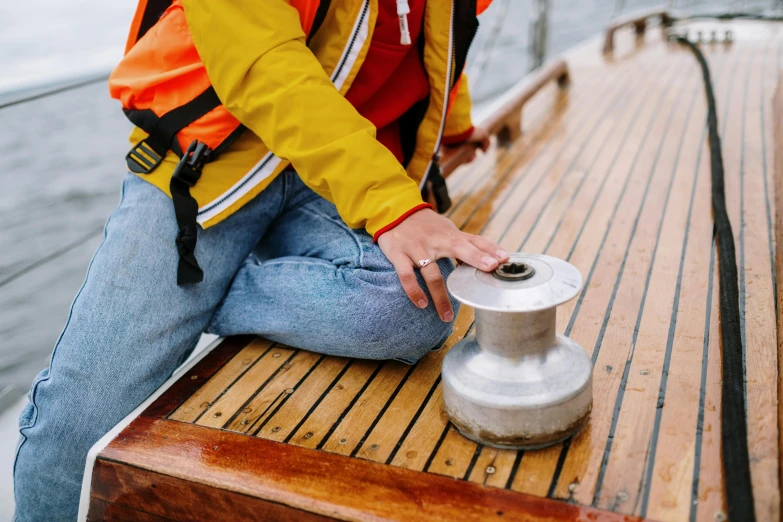 a woman in a life jacket sitting on a boat, trending on pexels, holding a golden bell, on a wooden table, round about to start, grey