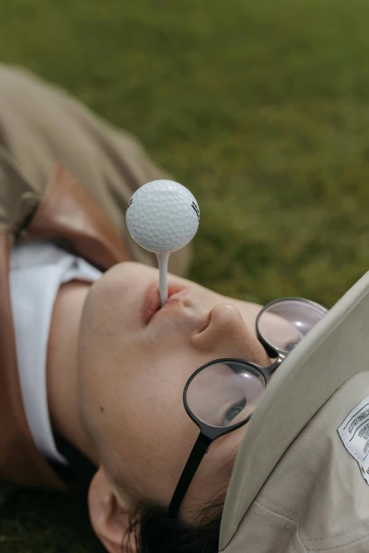 a man laying on the ground with a golf ball on his head, hooked nose, shades, skewed shot, spoon placed