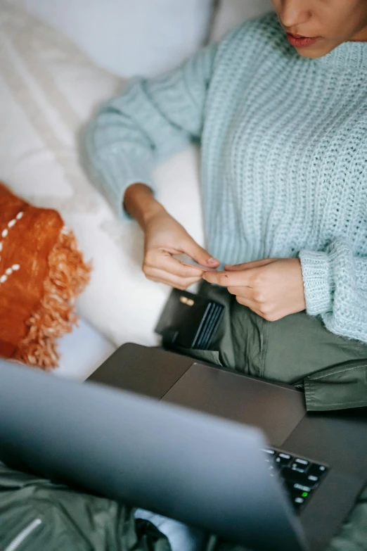 a woman sitting on a bed using a laptop, trending on pexels, with two front pockets, blue sweater, highly detailded, soft colours