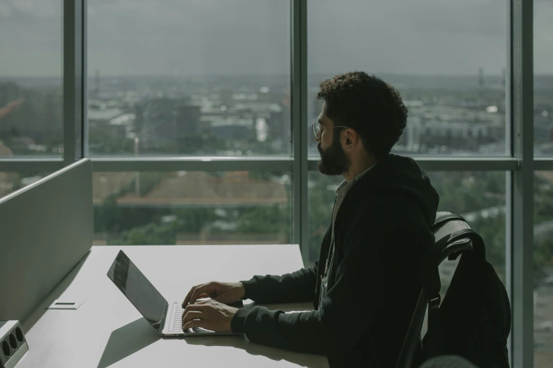 a man sitting at a table with a laptop, pexels contest winner, tech city in the background, ignant, background image, standing near a window