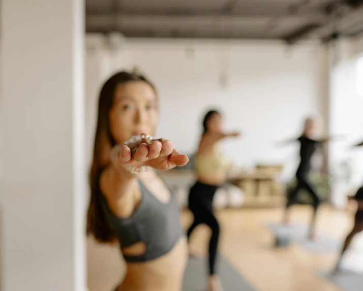 a group of women standing on top of a yoga mat, a picture, trending on pexels, arabesque, blurry focus, looking from shoulder, manuka, holding it out to the camera