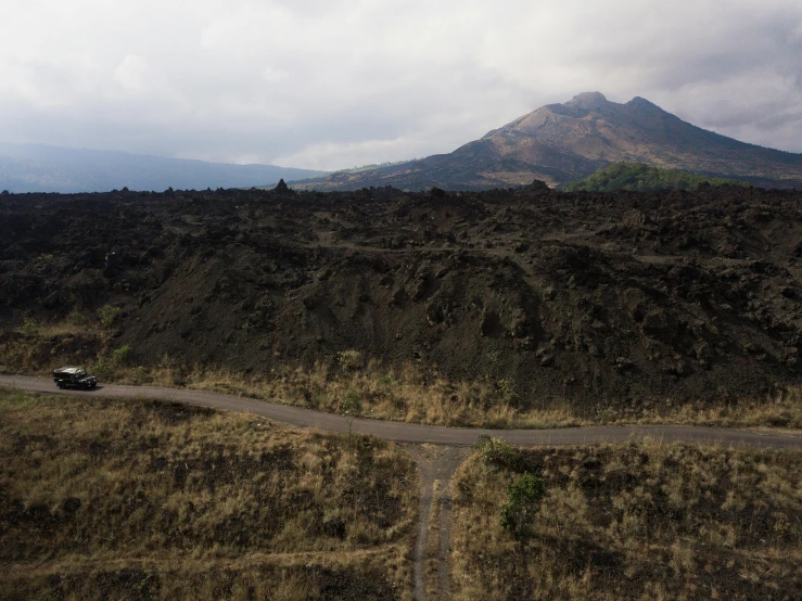 a car driving down a road with a mountain in the background, an album cover, unsplash, mingei, found on a volcano, background image, bali, flora-lush-crater