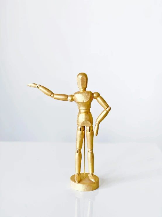 a gold figurine stands on a white surface, by Maggie Hamilton, unsplash, made of wood, hero action pose, midcentury modern, back and standing