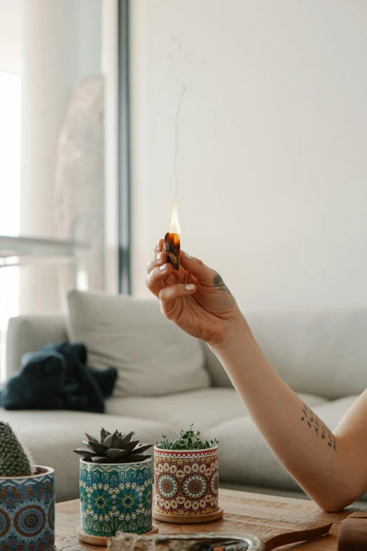 a woman sitting at a table holding a lit candle, inspired by Elsa Bleda, trending on pexels, on a couch, marijuana smoke, flame thrower, sustainable materials