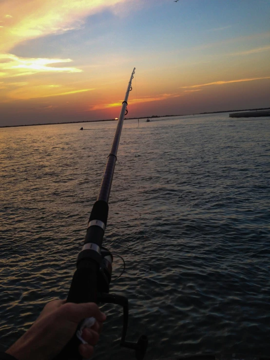 a person holding a fishing rod near a body of water, in the evening, upclose