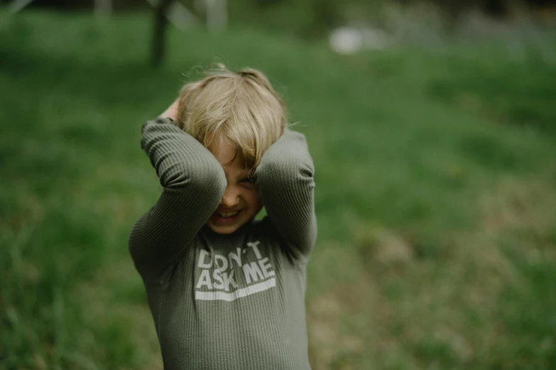 a little boy that is standing in the grass, by Emma Andijewska, pexels contest winner, hands shielding face, kaki body suit, sweat, winking