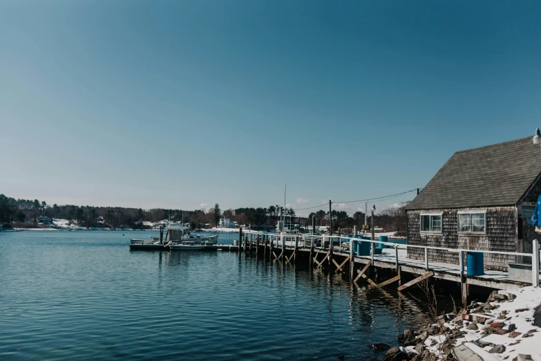 a man standing on a dock next to a body of water, new england architecture, unsplash photography, fishing town, clear blue skies