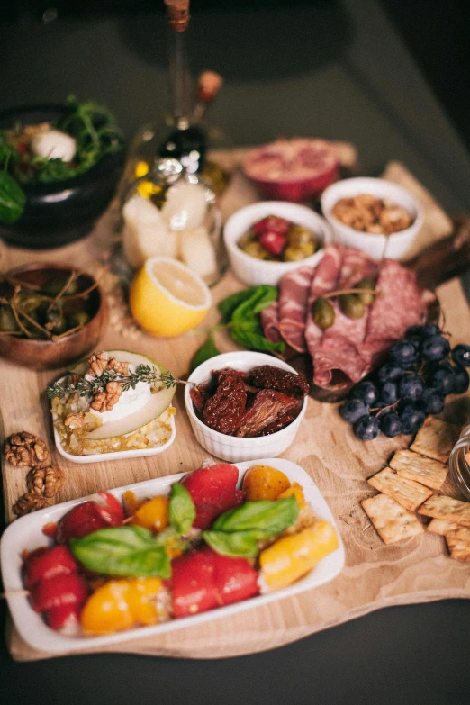 a wooden cutting board topped with different types of food, a still life, plates of fruit, olives, lit up, grazing