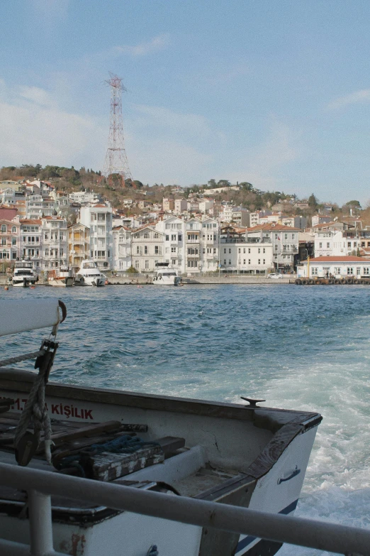 a boat on a body of water with a city in the background, by Niyazi Selimoglu, slide show, hydra, grayish, full frame image