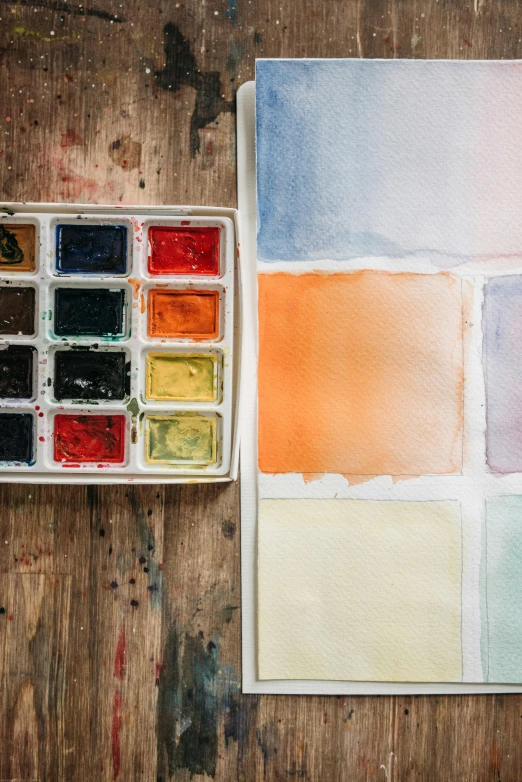 a watercolor palette sitting on top of a wooden table, inspired by Agnes Martin, trending on unsplash, square shapes, ((water color)), industrial colours, ( watercolor )