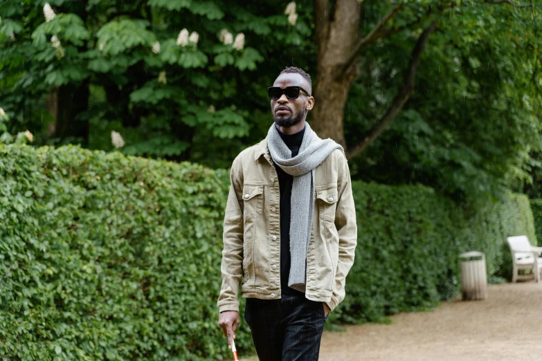 a man walking down a path with an umbrella, inspired by Theo Constanté, unsplash, sunglasses and a scarf, adut akech, standing in a botanical garden, wearing a jeans jackets