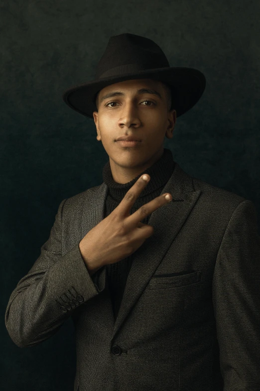 a man in a suit and hat poses for a picture, an album cover, inspired by Randy Vargas, trending on pexels, harlem renaissance, hand gesture, androgynous male, thiago alcantara, portrait shot 8 k