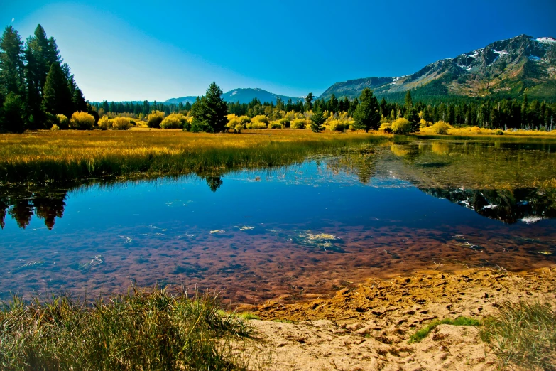a body of water with a mountain in the background, inspired by Ethel Schwabacher, land art, big bear lake california, sunny meadow, phot, colorful”