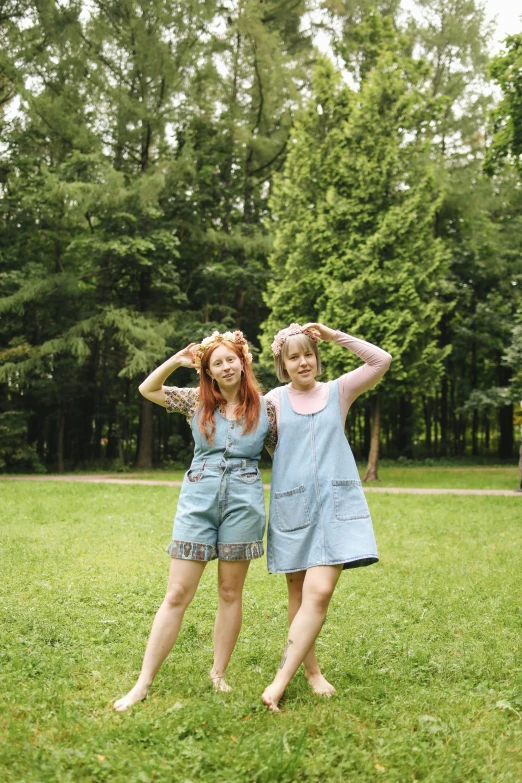 a couple of women standing on top of a lush green field, by Aguri Uchida, pexels, blue overalls, one is a redhead, in a park, lookalike