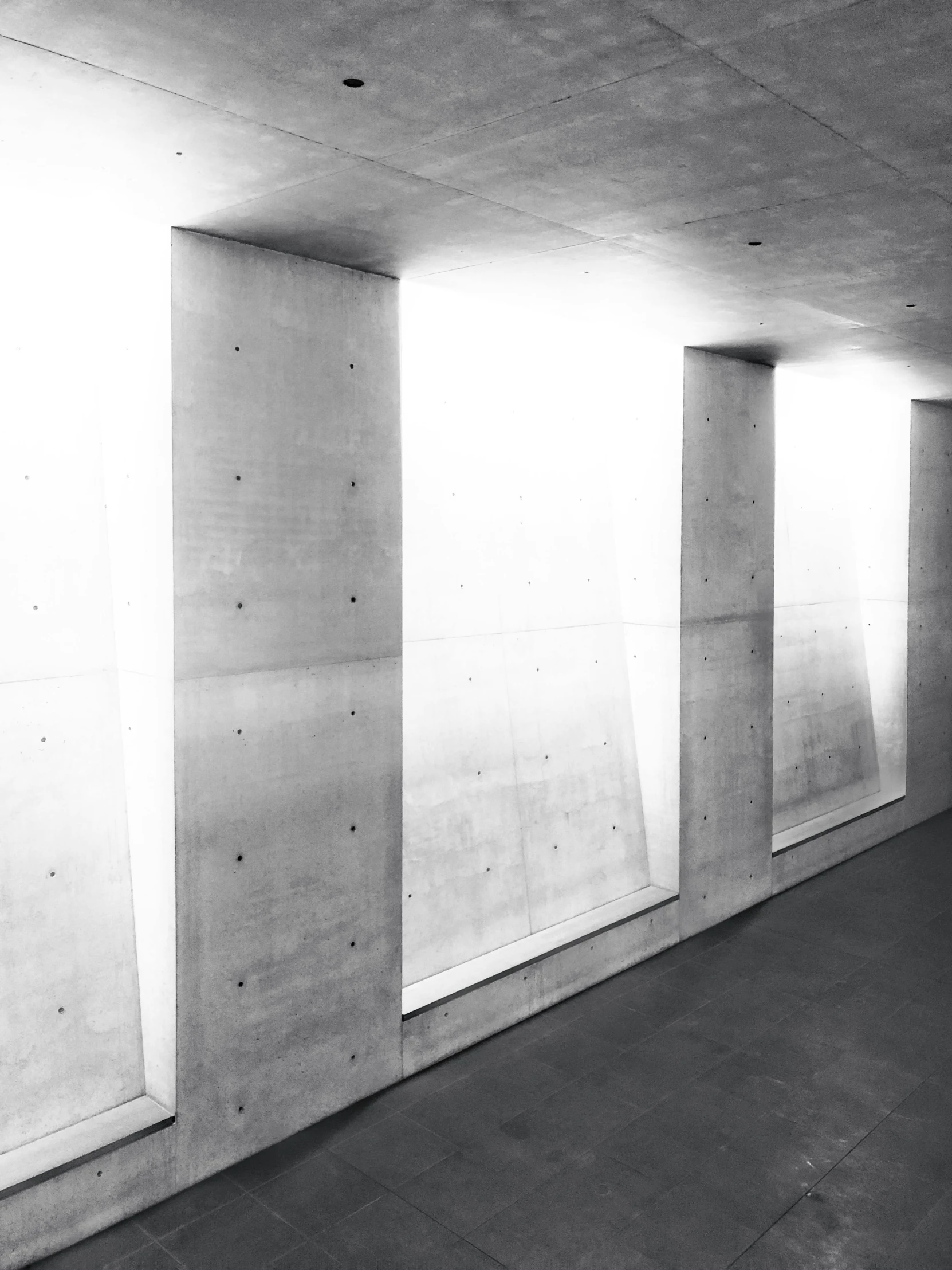 a man riding a skateboard up the side of a ramp, a black and white photo, inspired by Tadao Ando, unsplash, light and space, inside a crypt, rows of windows lit internally, herzog de meuron, solid concrete