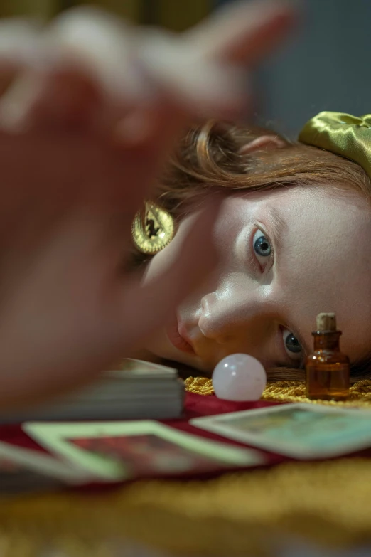 a close up of a child laying on a table, a hyperrealistic painting, inspired by Gerrit Dou, magic realism, sadie sink, fortune teller, ignant, shot from cinematic